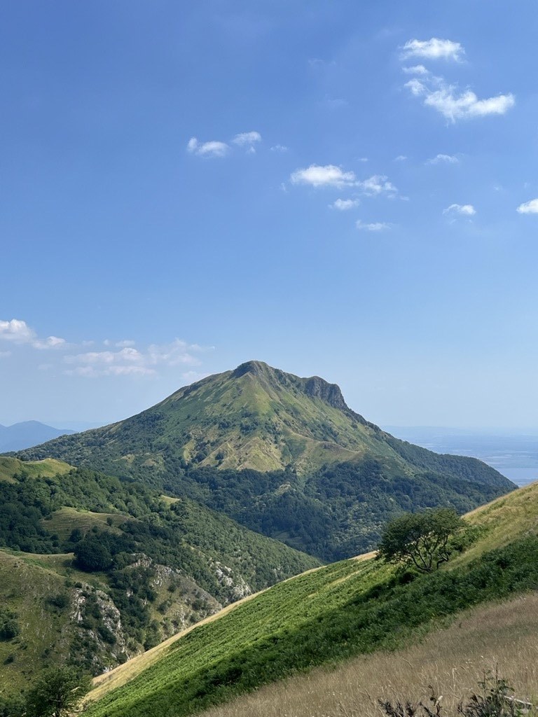 Green slopes and the summit ridge of Monte Prana under a clear sky, with the sea faint on the horizon.