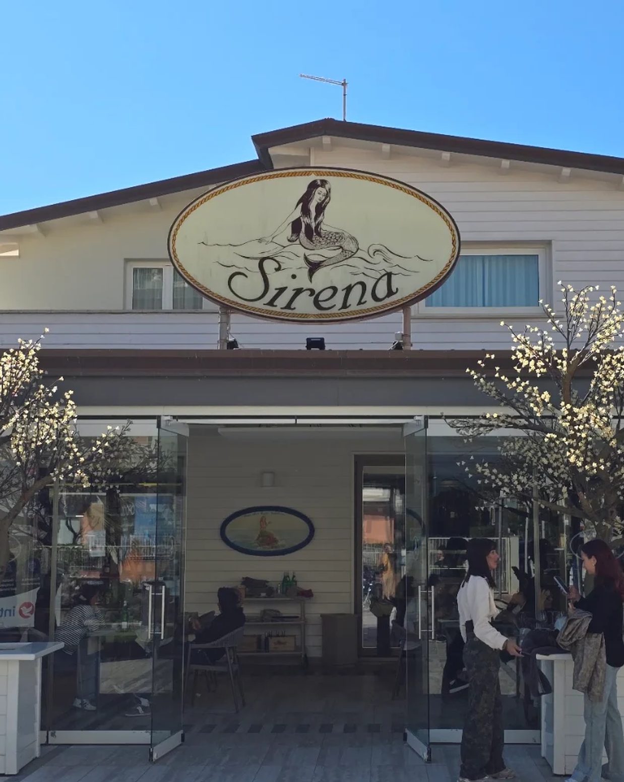 The white entrance of Caffè Sirena on the Lido di Camaiore promenade, with blossom trees either side.
